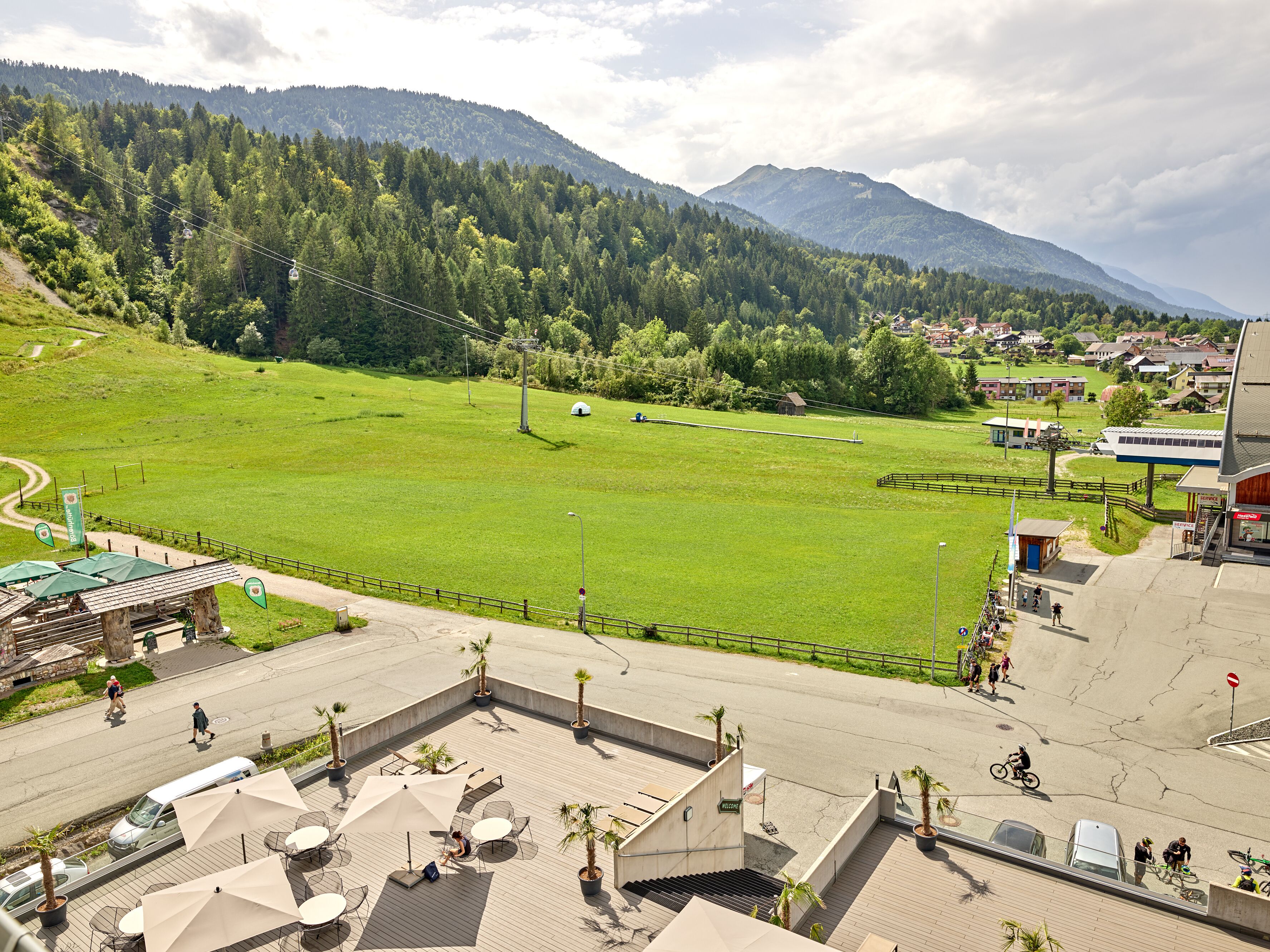 A hotel with outdoor seating, a view of a green field, and a mountain in the background.