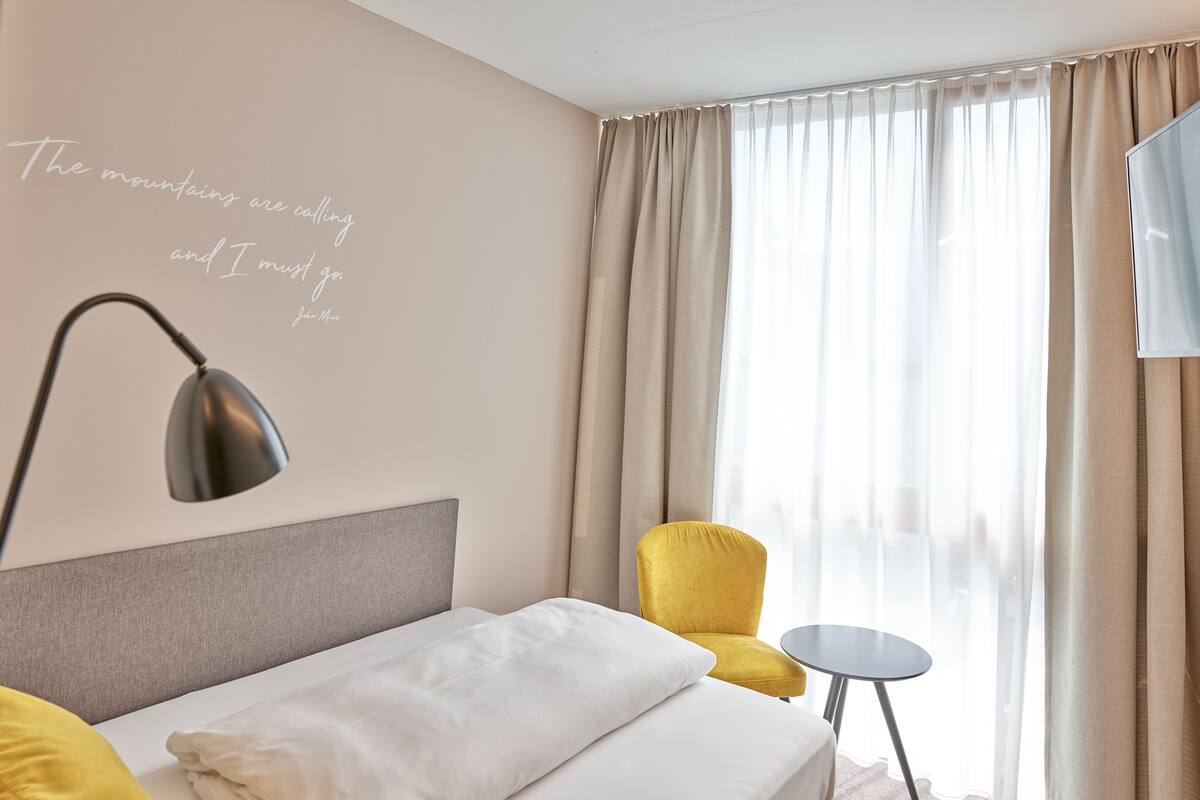 Habitación de hotel con cama, escritorio, silla y ventana con cortinas.