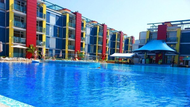 A swimming pool with a tiled edge, surrounded by a multi-story building with balconies and a blue canopy structure. - Menada Elit IV Apartments (Sunny Beach)