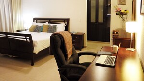 A hotel room with a bed, a desk with a laptop, a chair, a nightstand, a lamp, and a door. - Pelicanos 112 (Playa del Carmen)