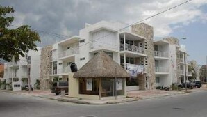 A multi-story building with balconies, a thatched-roof structure, and a paved street. - Pelicanos 112 (Playa del Carmen)