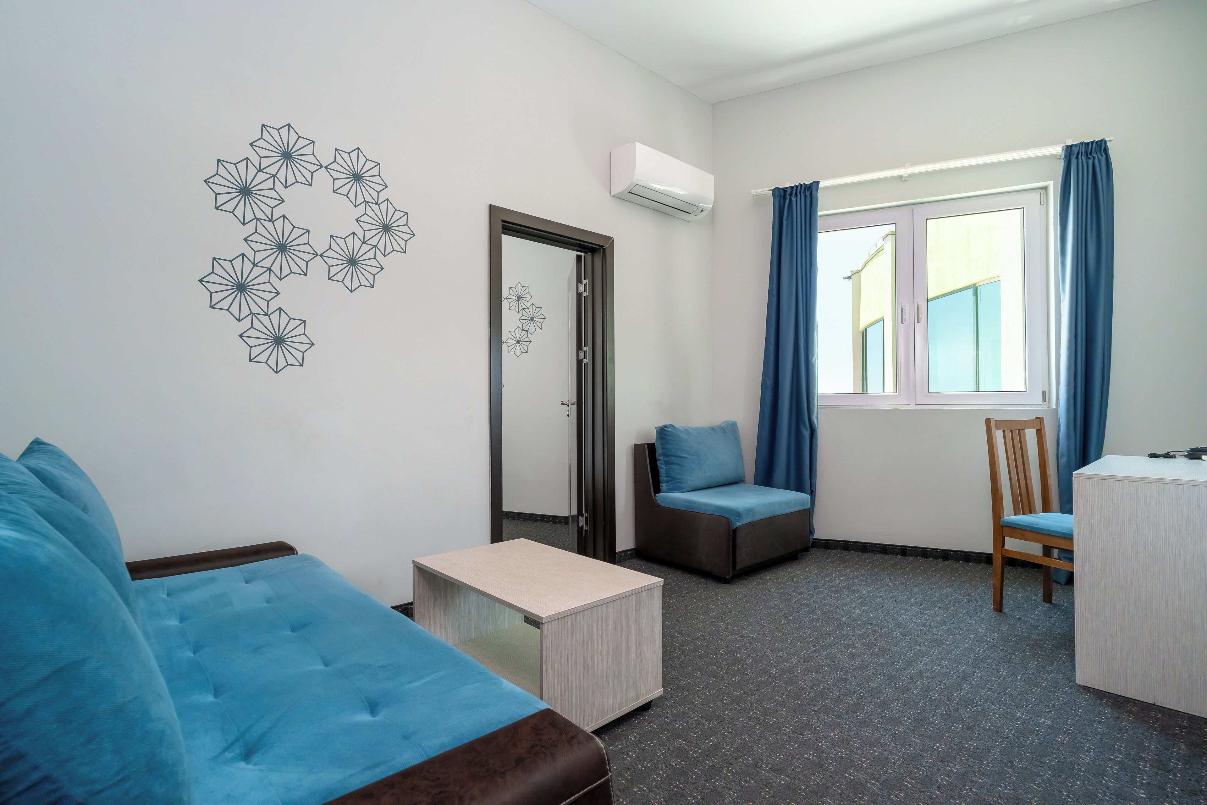 A room with a blue sofa, a small table, a chair, and a window with curtains.