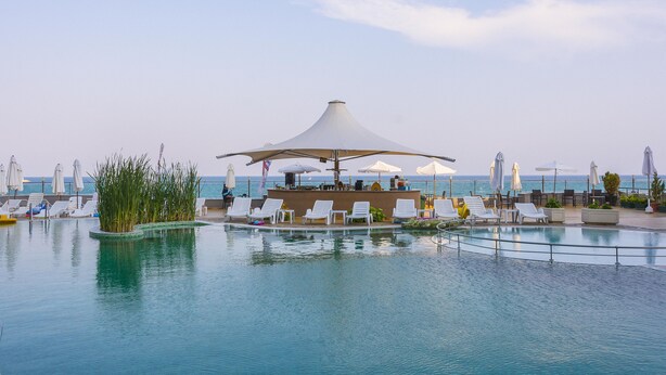 A pool area with lounge chairs and umbrellas, a bar, and a view of the sea. - MPM Hotel Arsena (Nessebar)