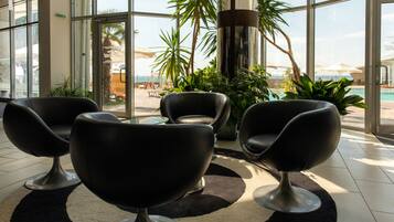 Un hall d’entrée moderne avec des fauteuils en cuir noir, une grande porte vitrée donnant accès à un espace piscine et des plantes d’intérieur.