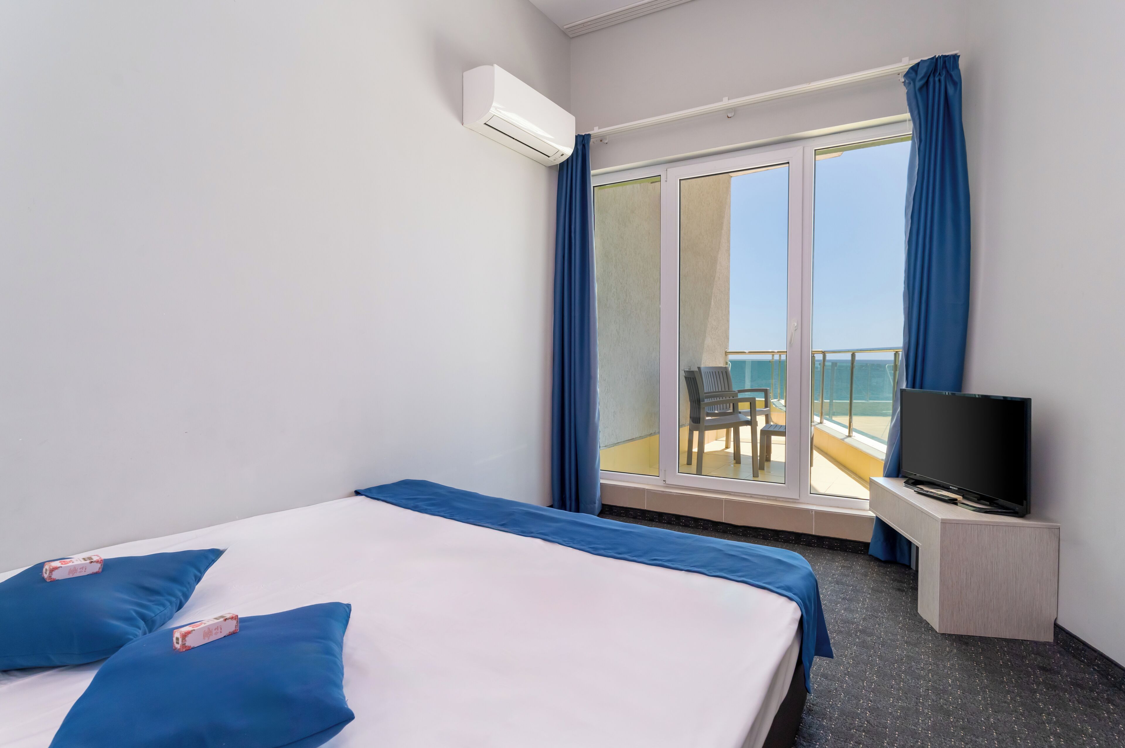 Una habitación de hotel con cama, televisión sobre un mueble y balcón con una silla.
