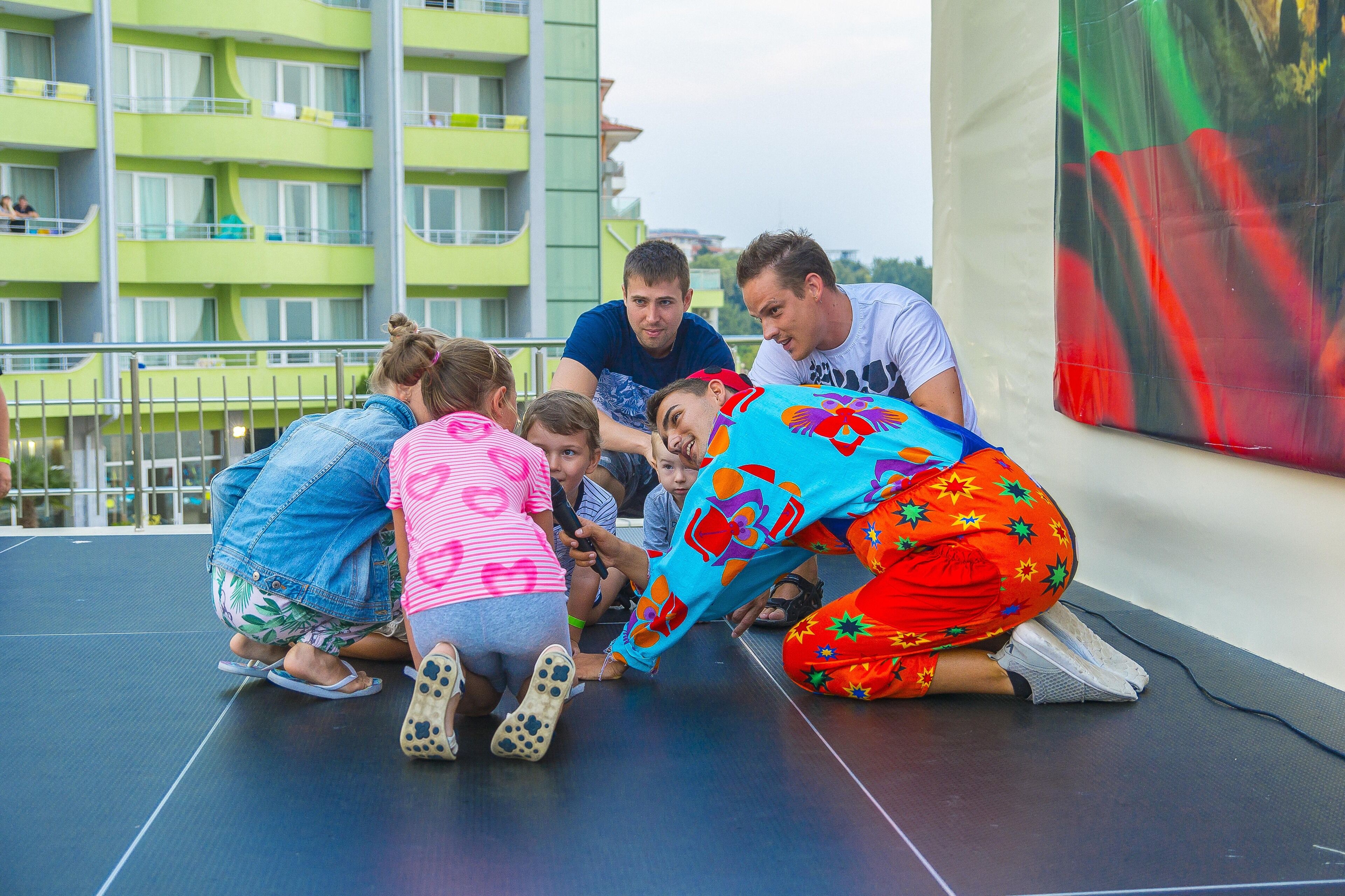 Un gruppo di persone sedute su un palco con un edificio verde sullo sfondo.