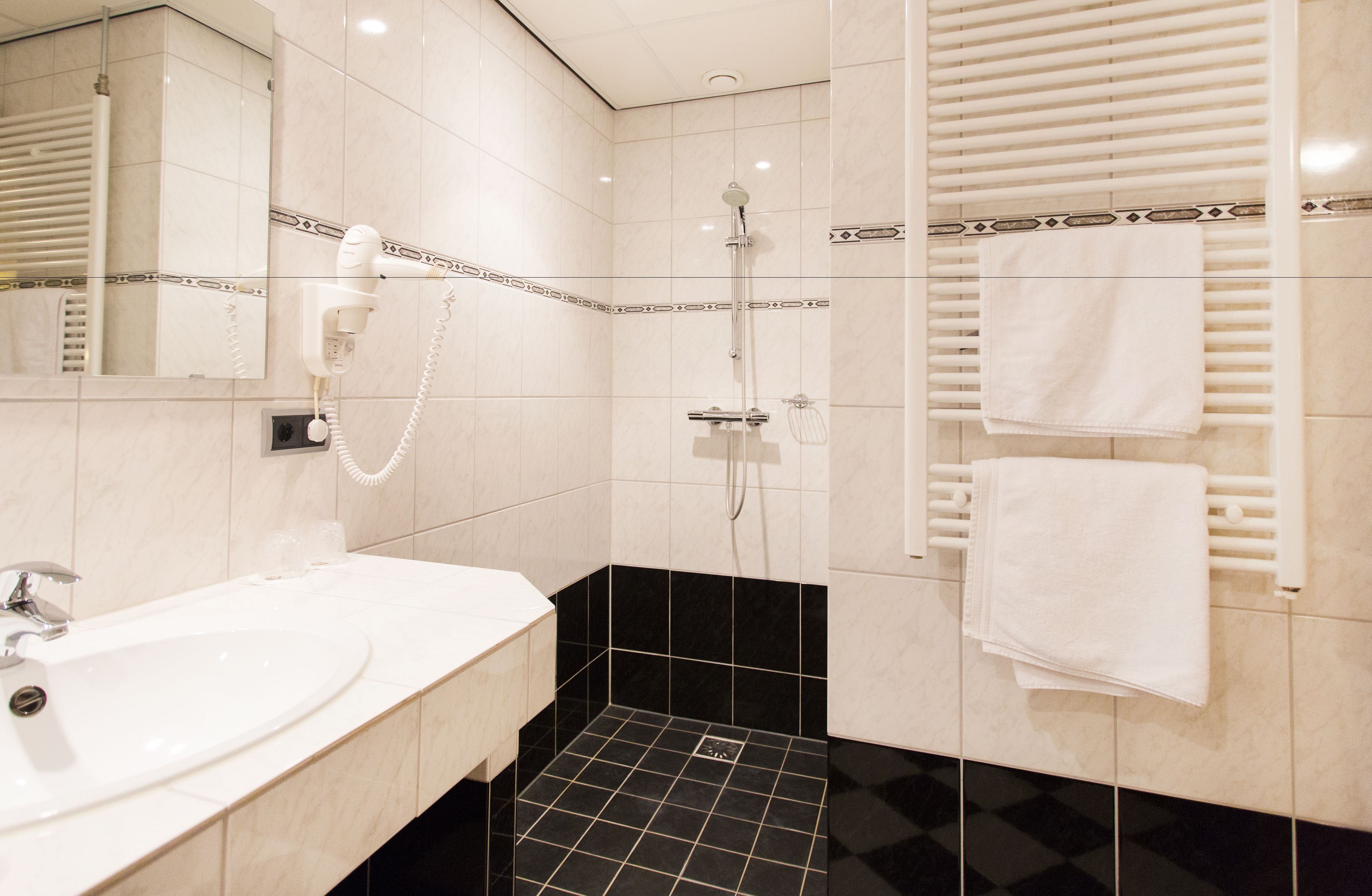 A modern bathroom with a white sink, a handheld hair dryer, a shower with a handheld showerhead, and a towel rack with towels.