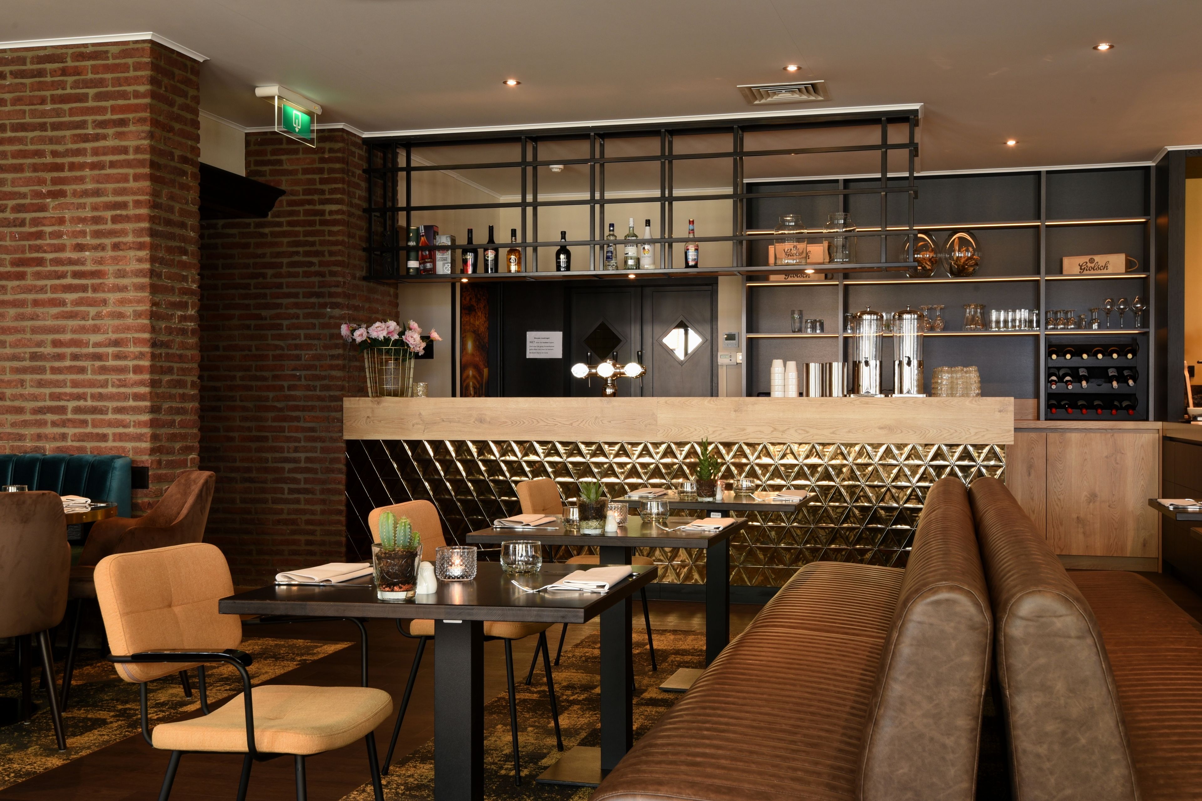 Een restaurant met een bakstenen muur, een barzone met flessenrekken en zitmogelijkheden, waaronder een lange bank en tafels.