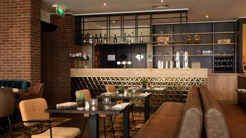 Een restaurant met een bakstenen muur, een barzone met flessenrekken en zitmogelijkheden, waaronder een lange bank en tafels.