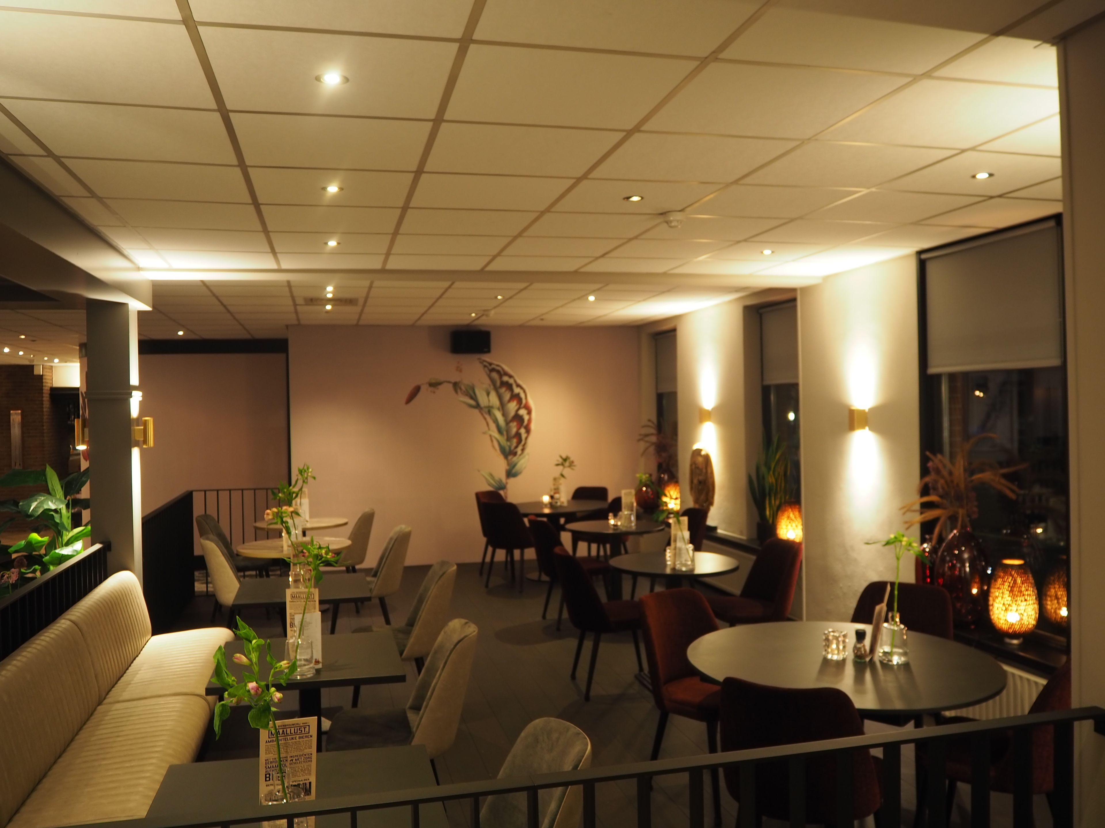 Ein Restaurant mit mehreren Tischen und Stühlen, einer Wand mit Dekoration und einer Decke mit eingelassener Beleuchtung.