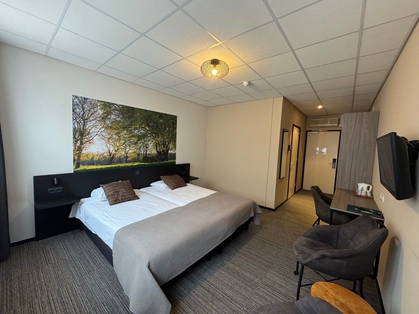 A hotel room with a bed, a desk, a chair, a television, and a painting on the wall.