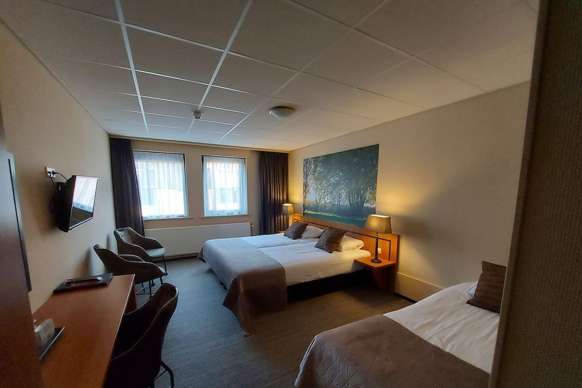 A hotel room with two beds, a desk, chairs, a TV, and a painting on the wall.