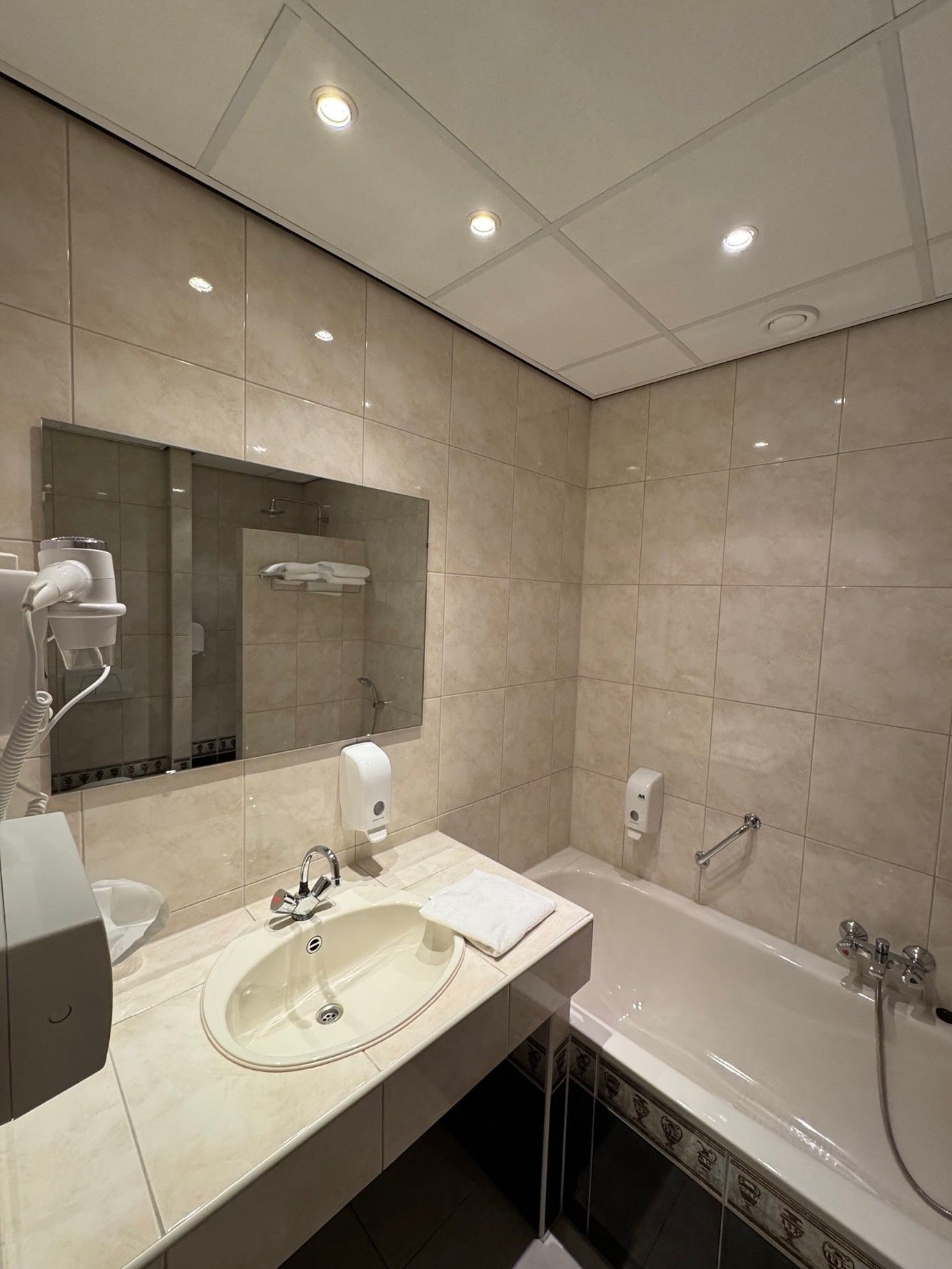 Un baño moderno con lavamanos, espejo, secador de pelo y bañera.
