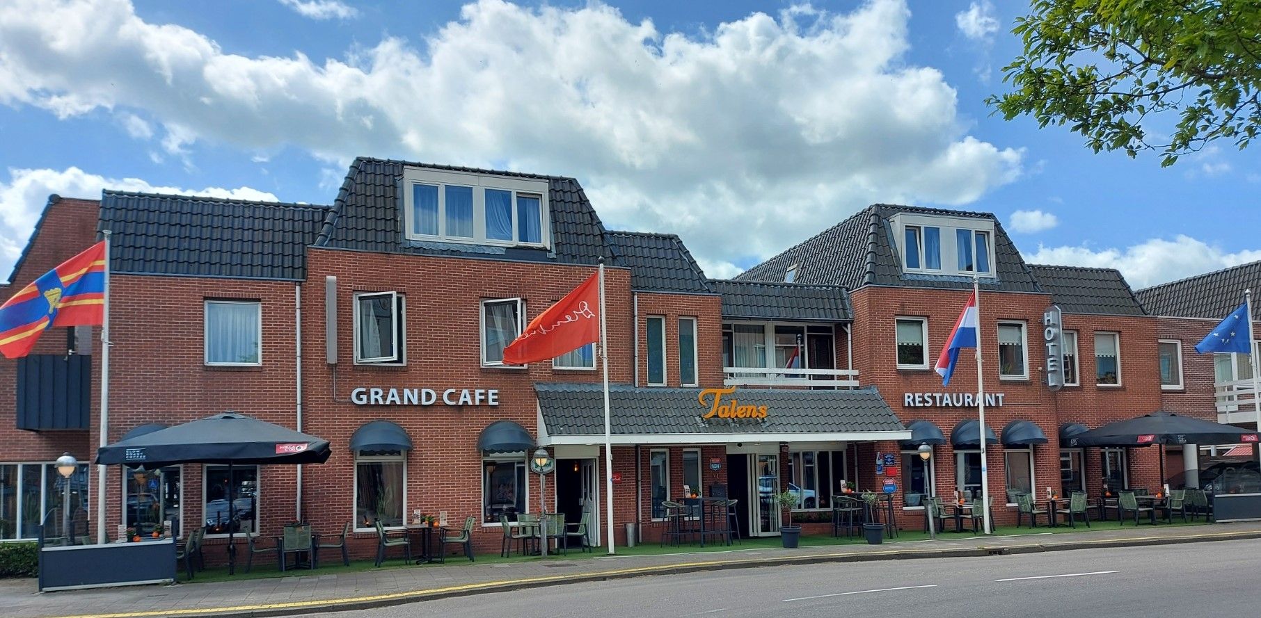 Um edifício de tijolos com um letreiro indicando 'Grand Cafe' e 'Talens Restaurant' no andar térreo.