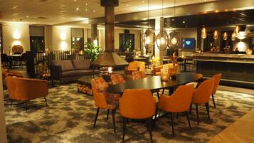 A modern hotel lobby with a central seating area, a bar, and a fireplace.