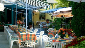 An outdoor dining area with tables and chairs, covered by striped umbrellas, and surrounded by potted plants and flowers. - Hôtel Restaurant le Pan de Bois (Breviandes)