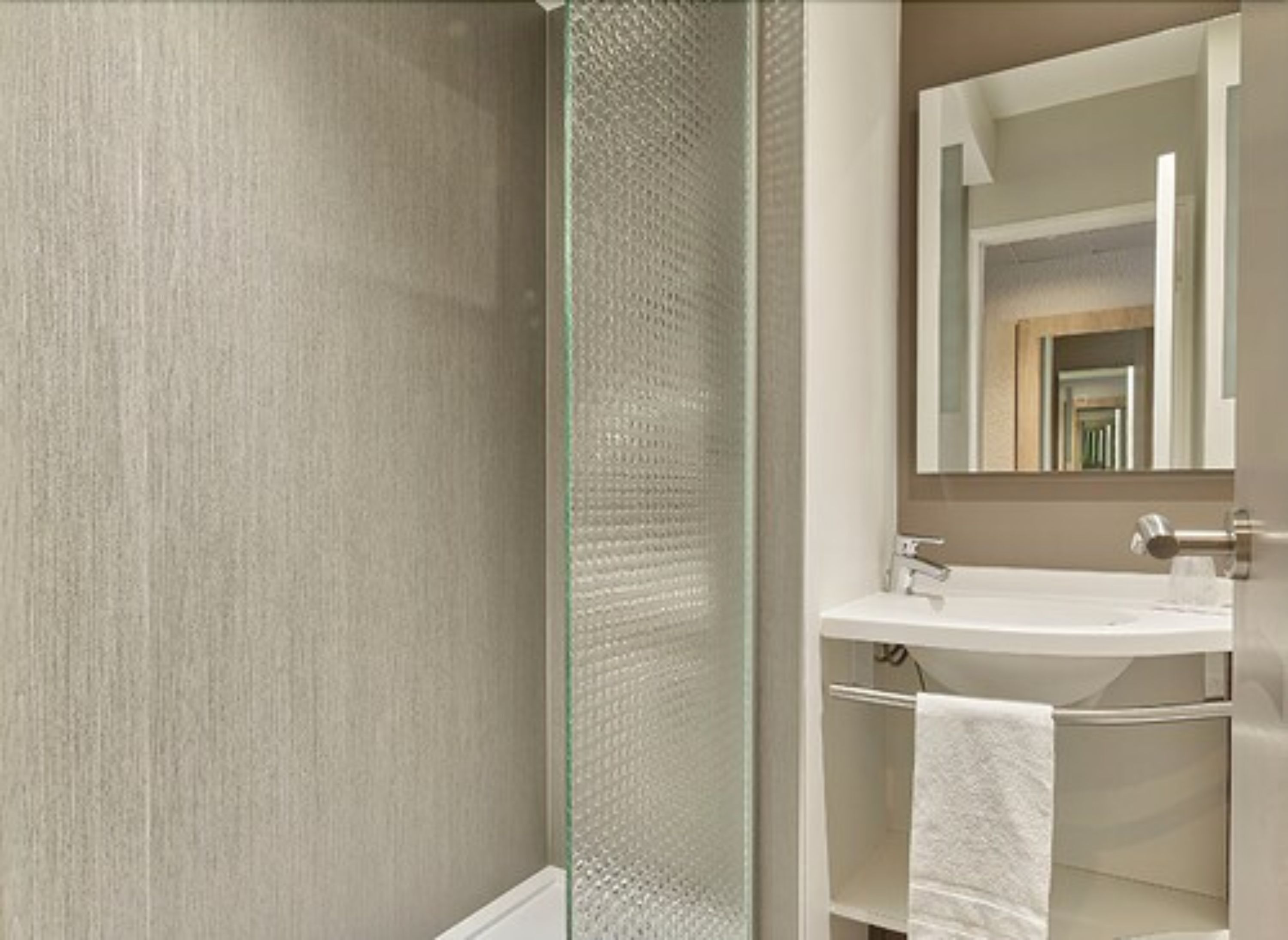 Un baño con mampara de vidrio, lavamanos blanco y espejo sobre él.
