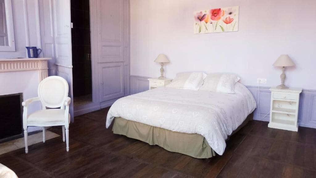 Un dormitorio con una cama grande, dos mesitas de noche, una silla y un cuadro en la pared.