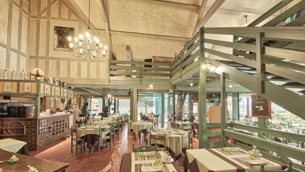 A restaurant with a high ceiling, exposed beams, and a mezzanine level. Tables are set with tablecloths and centerpieces. - Hôtel Restaurant le Pan de Bois (Breviandes)