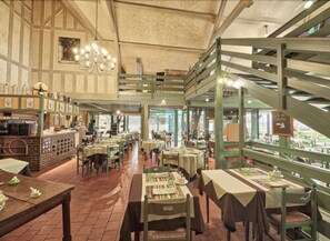 A restaurant with a high ceiling, exposed beams, and a mezzanine level. Tables are set with tablecloths and centerpieces. - Hôtel Restaurant le Pan de Bois (Breviandes)
