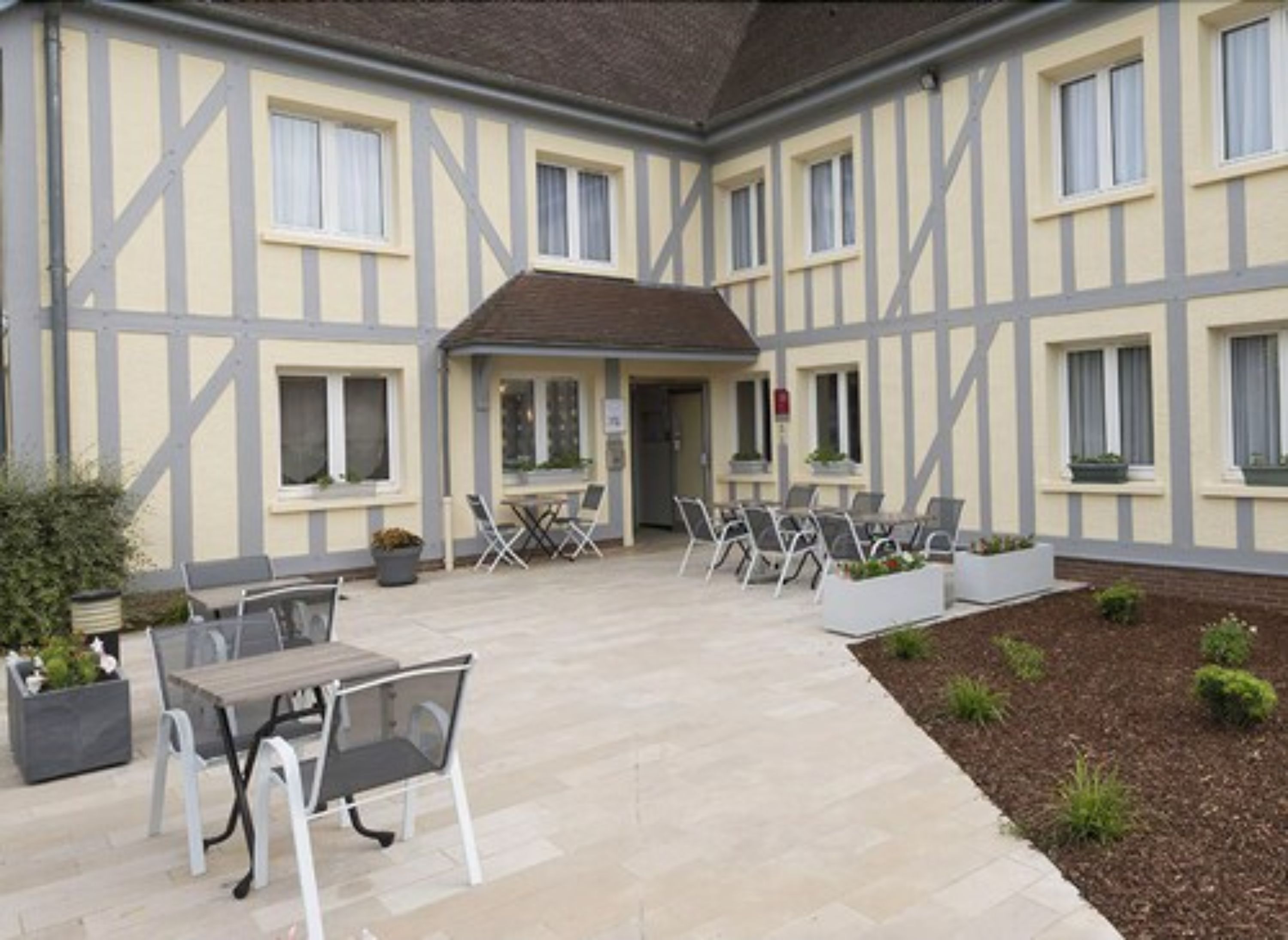 A courtyard with outdoor seating, a covered area, and a building with a timber-framed facade.