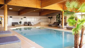 An indoor swimming pool with lounge chairs and a staircase leading to upper levels.