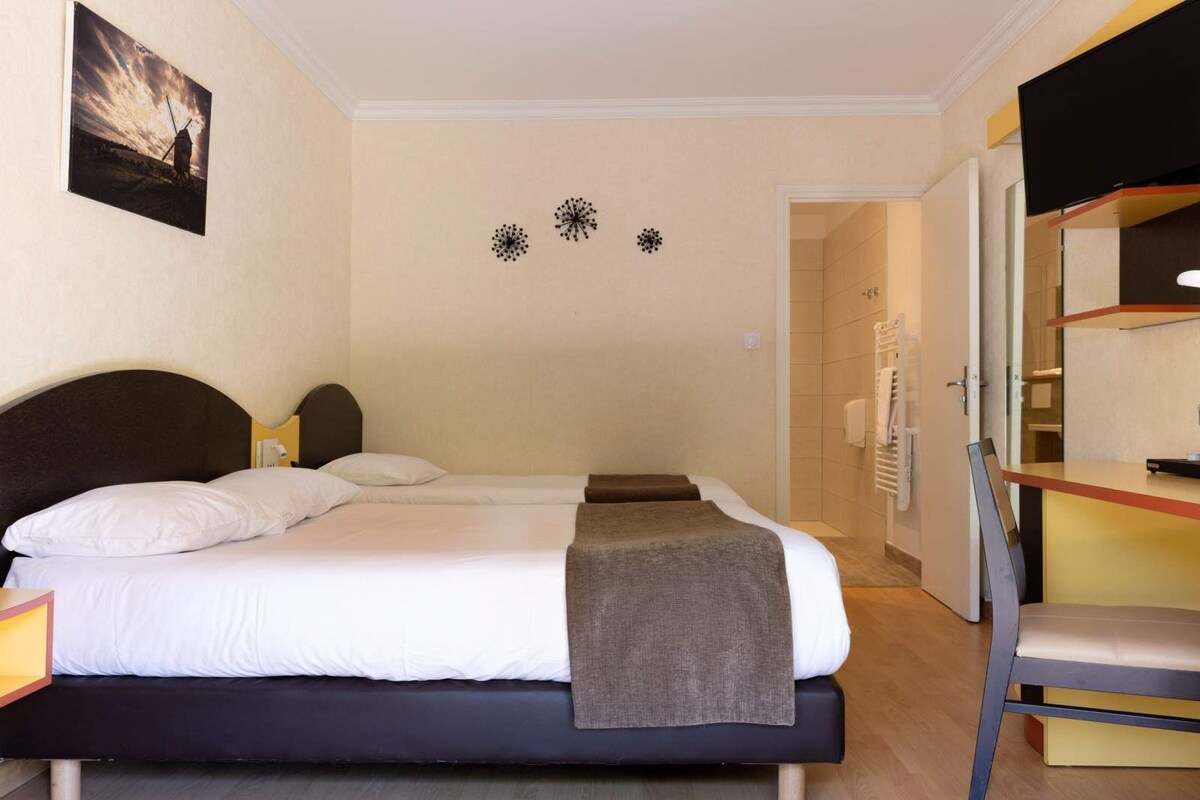 A hotel room with a bed, a desk, and a chair. There is a picture on the wall and a door leading to another room.
