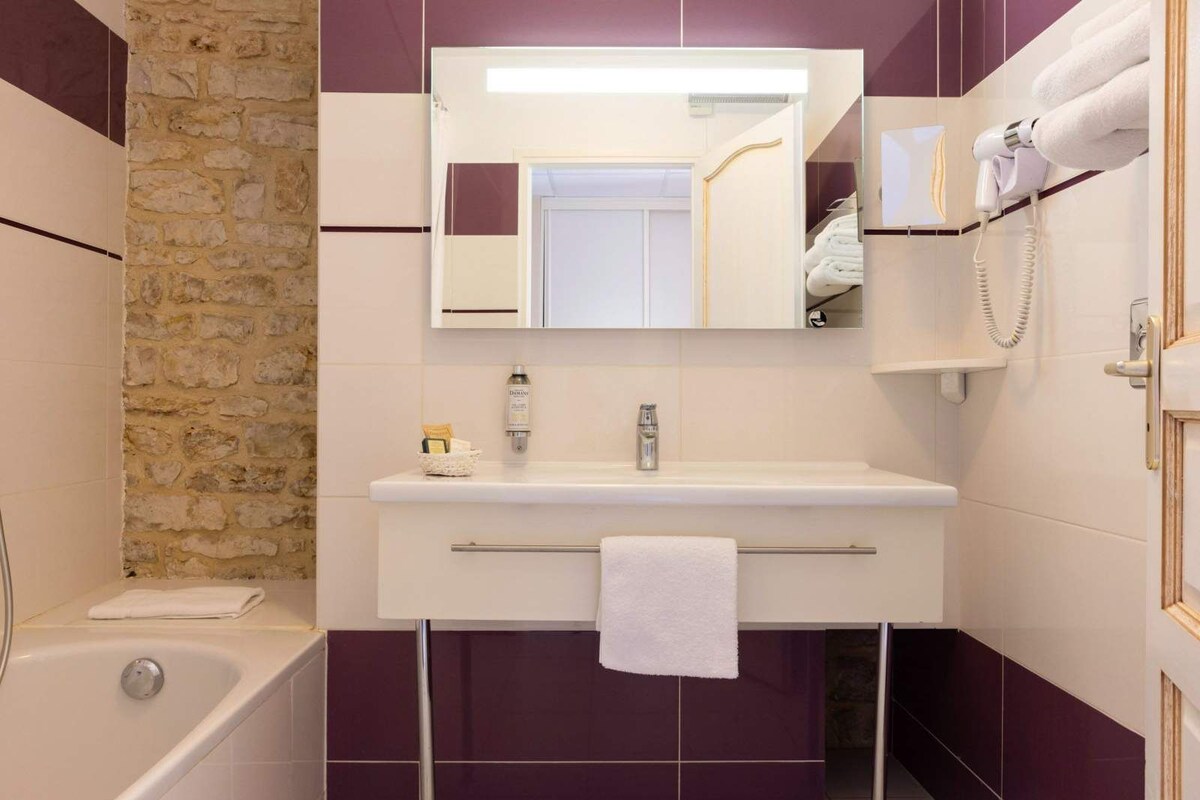 A bathroom with a stone wall, a white sink, a mirror, a towel rack, and a hairdryer.