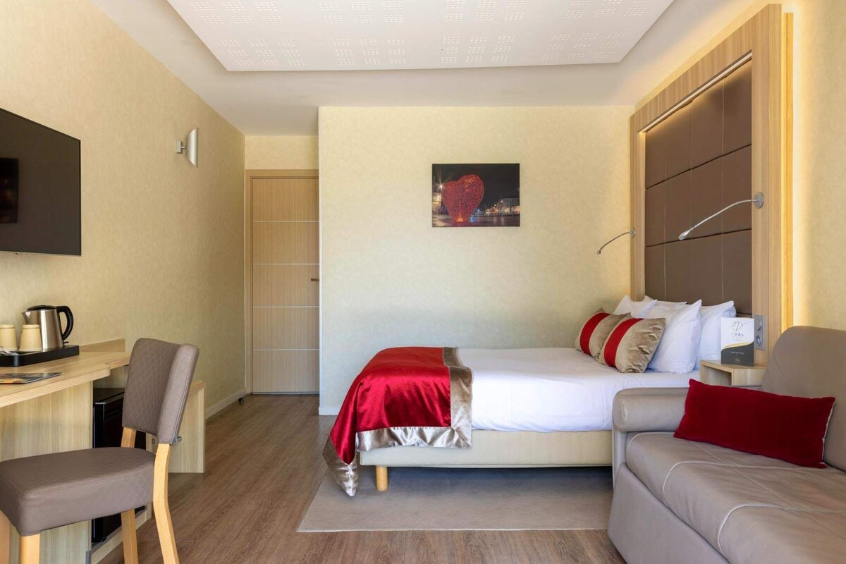 A hotel room with a bed, a desk, a chair, a sofa, and a television.