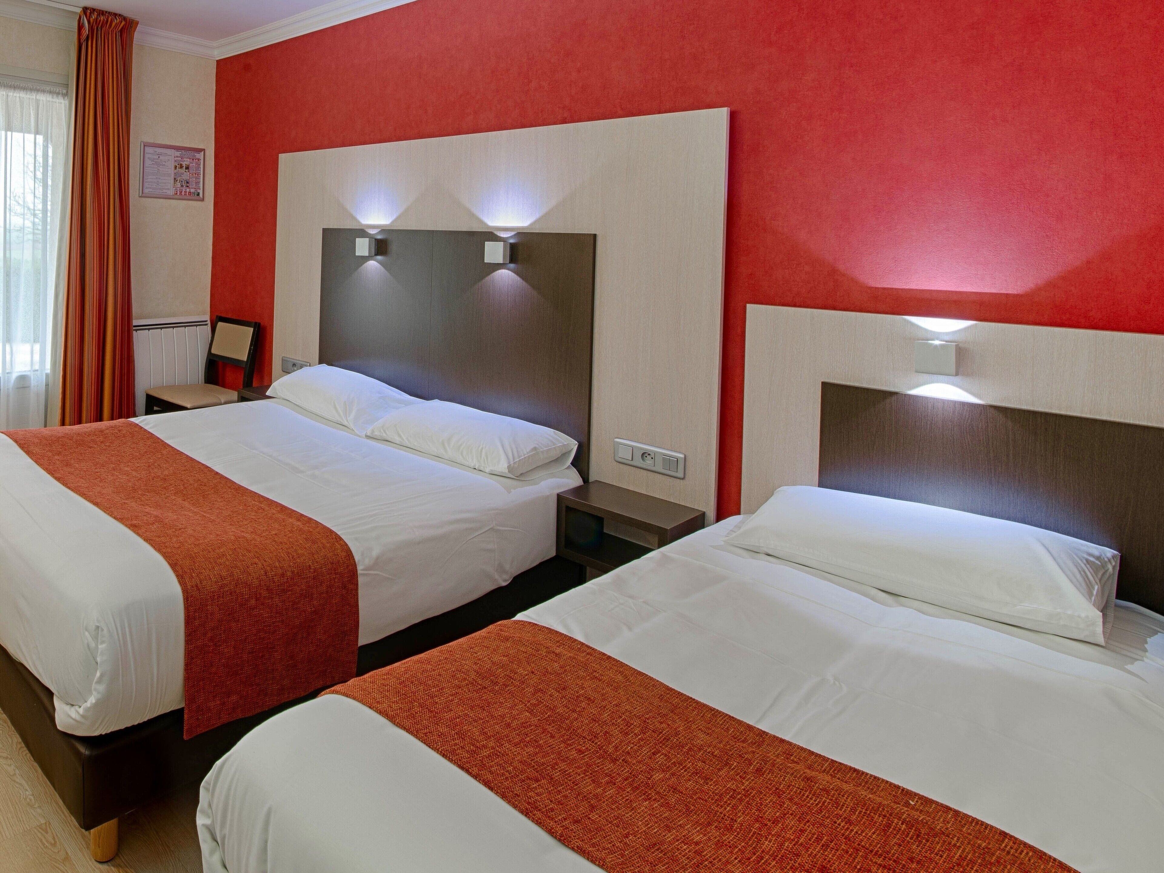 A hotel room with two beds, each with a headboard and bedside lamps.