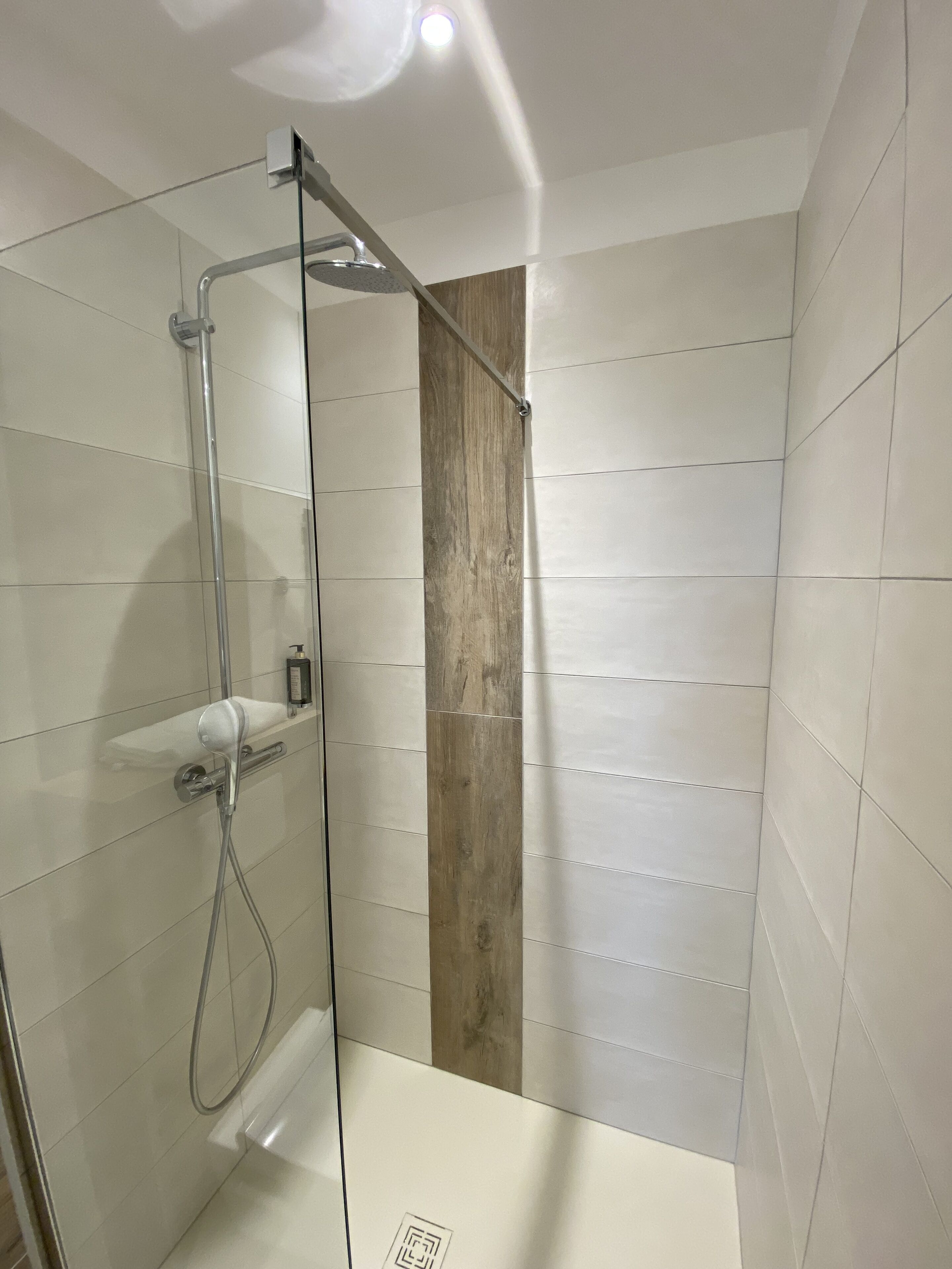 Eine begehbare, gläserne Dusche mit einer Wand aus Holz, einer Handbrause und einem wandmontierten Wasserhahn.