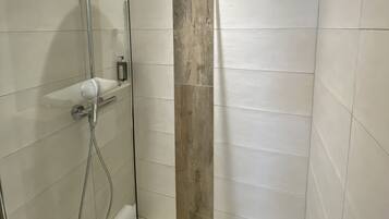 Eine begehbare, gläserne Dusche mit einer Wand aus Holz, einer Handbrause und einem wandmontierten Wasserhahn.