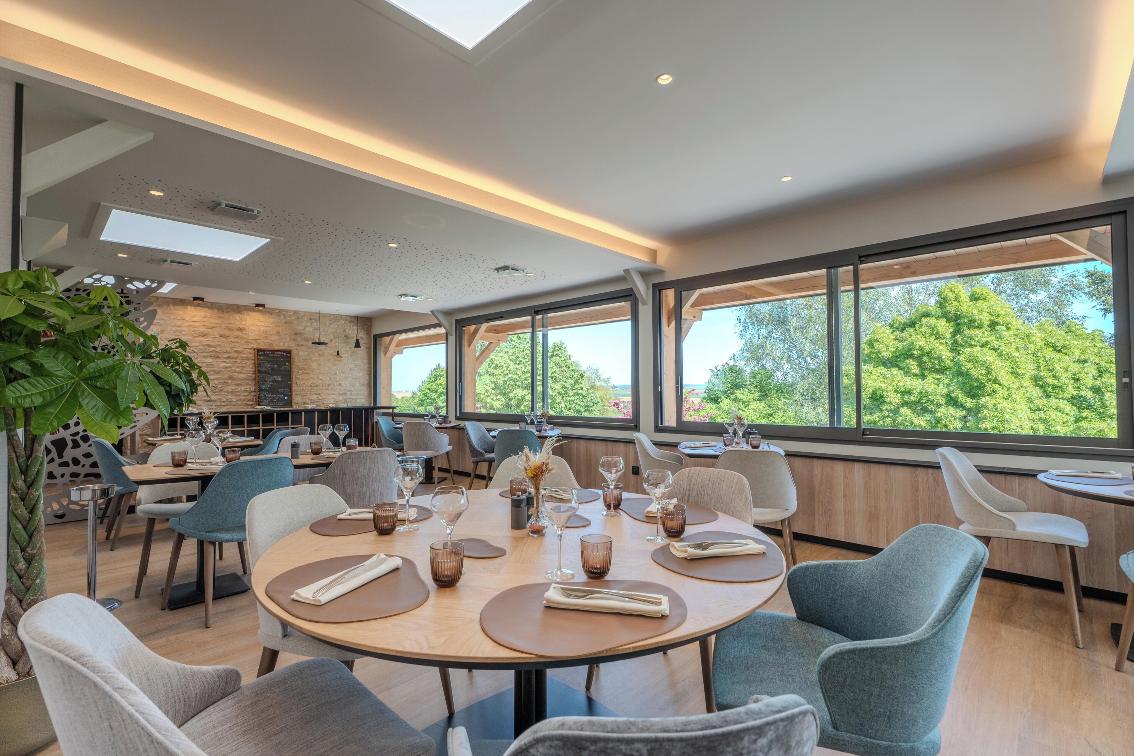 Un espace repas moderne avec des tables rondes, des chaises et de grandes fenêtres donnant sur la verdure.