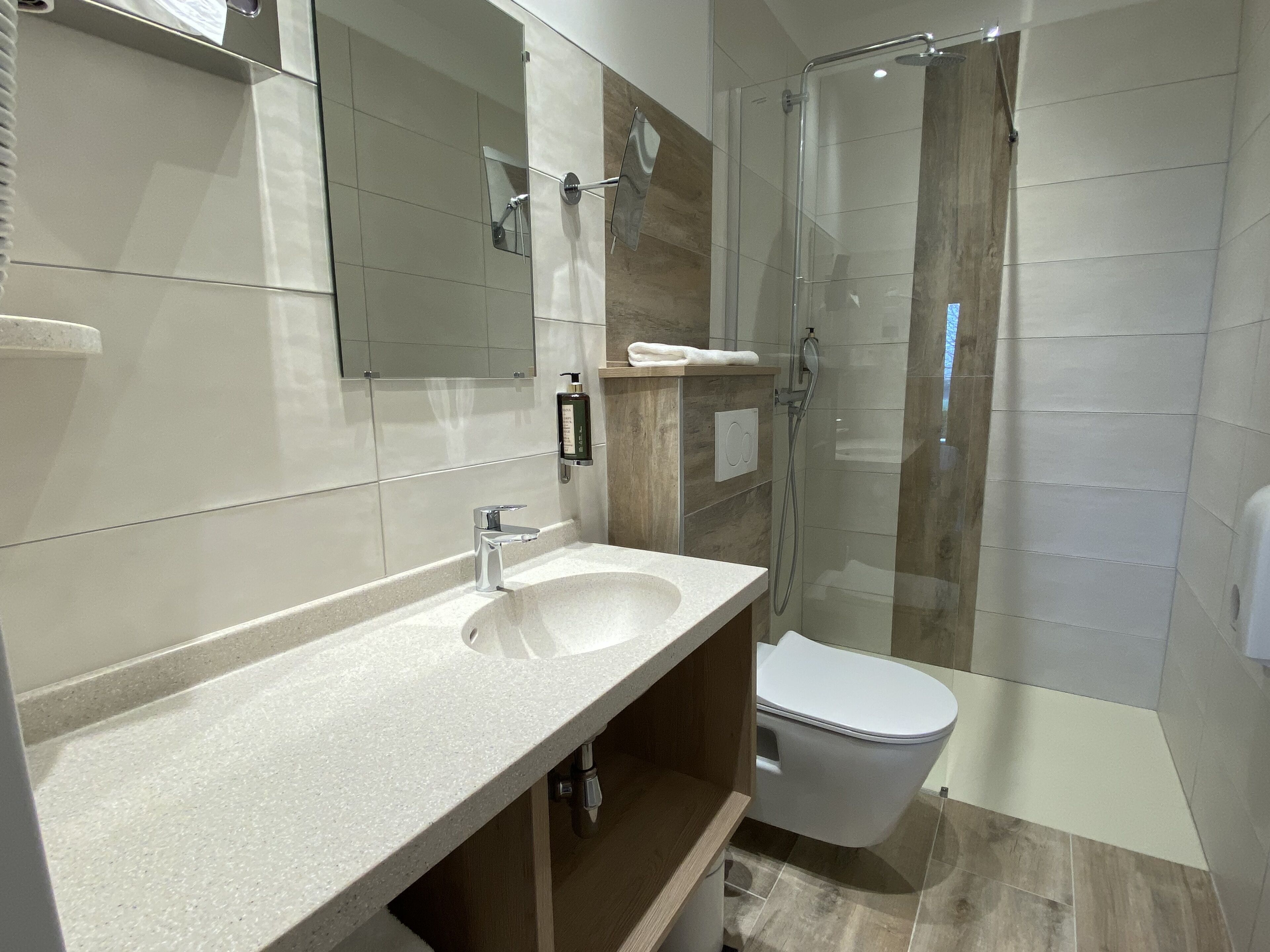 Une salle de bain moderne avec un grand miroir, un lavabo, des toilettes et une douche à parois de verre.