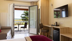 A modern hotel room with a bed, a desk, a chair, a television, and a sliding glass door leading to an outdoor area with a table and chairs.