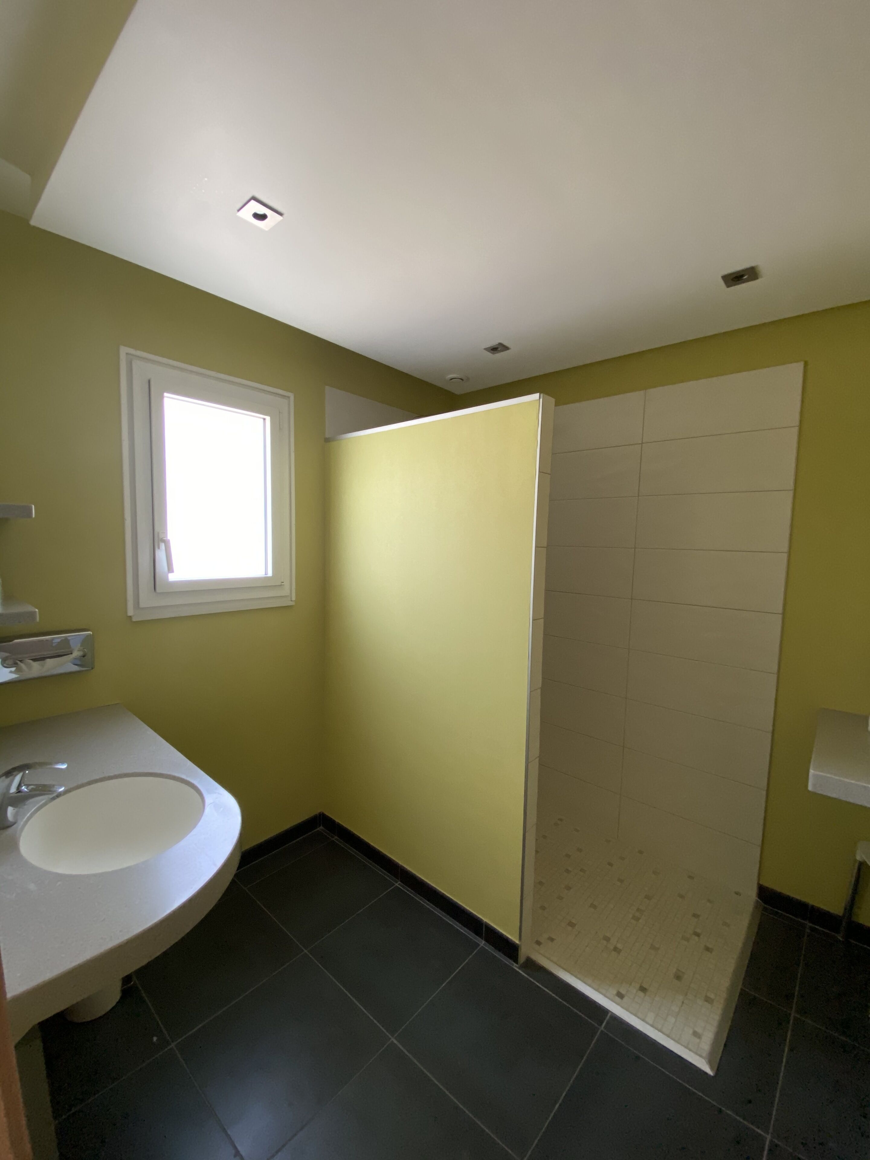 Une salle de bain avec un lavabo blanc, une fenêtre, une douche et un sol carrelé.