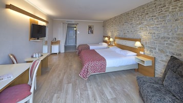 A hotel room with two beds, a desk with a chair, a television, and a stone wall.