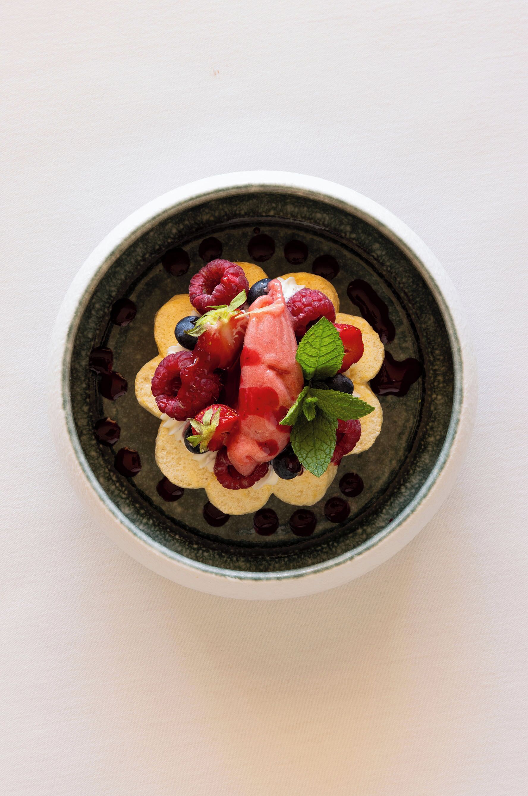 A dessert with berries and mint leaves on a plate.