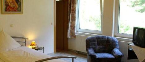 A bedroom with a bed, a chair, a television, and a window with curtains.