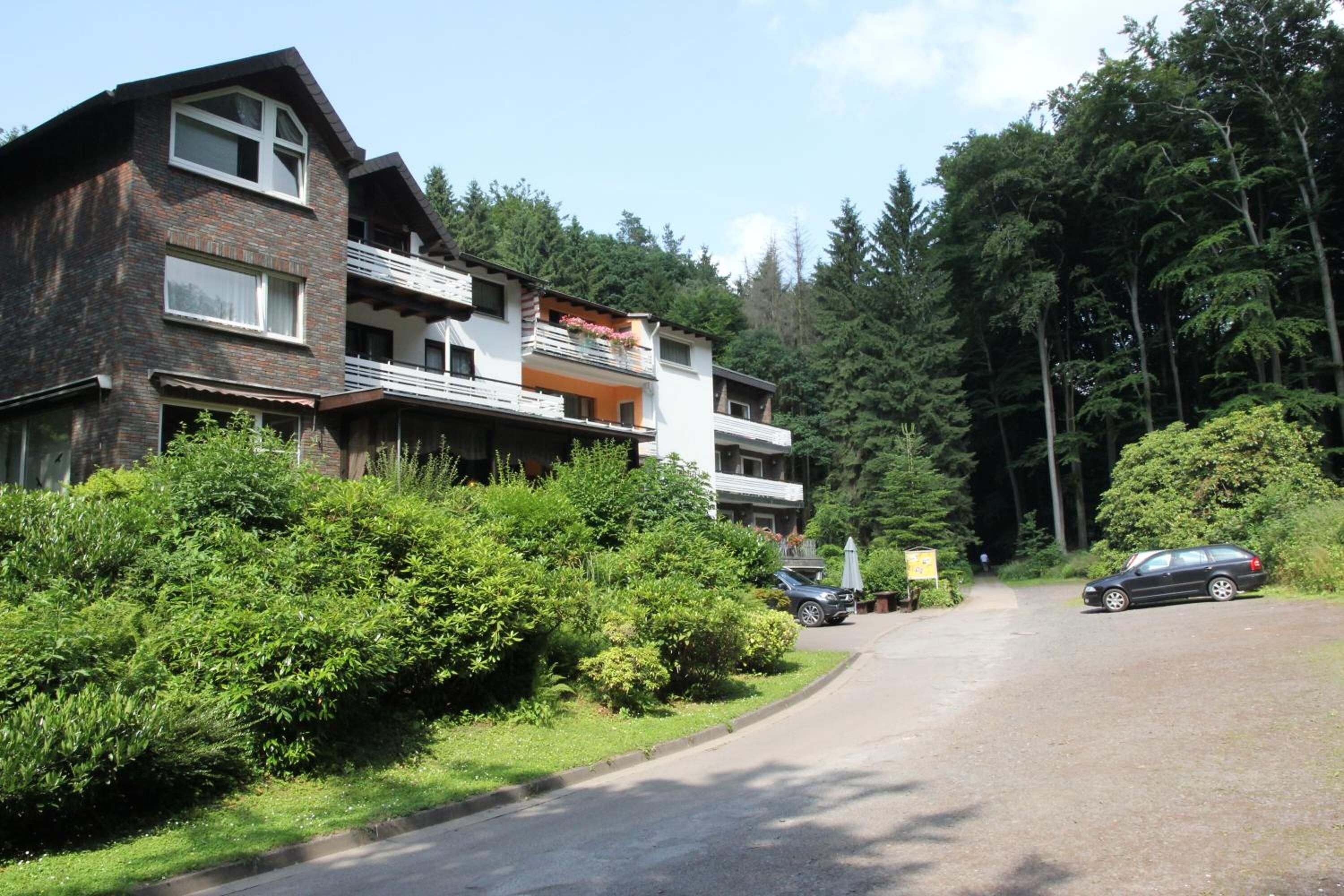 A multi-story residential building with balconies, surrounded by dense greenery and tall trees.
