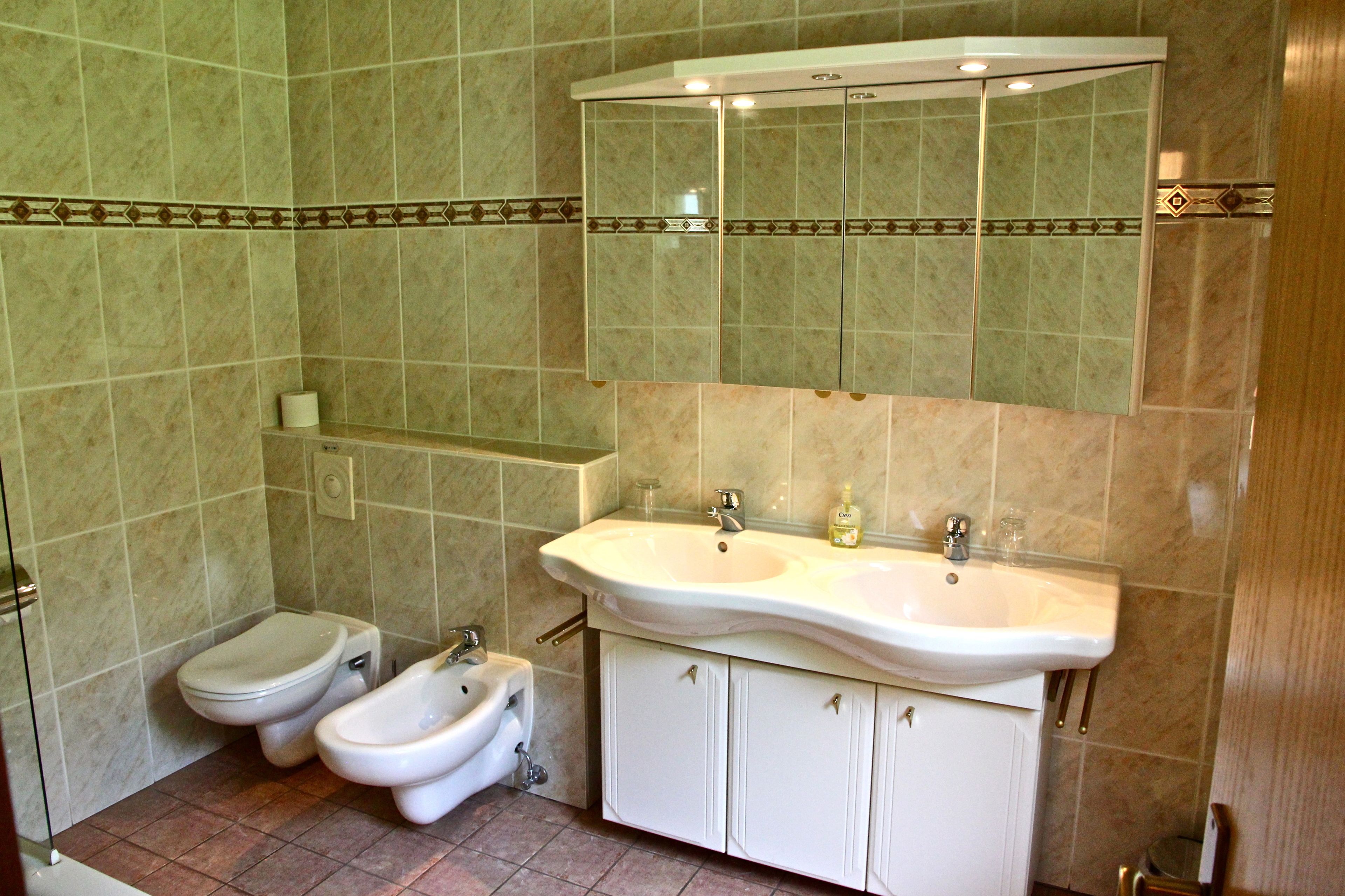 Un baño con dos inodoros, un bidé, un lavamanos y un espejo sobre el lavamanos.