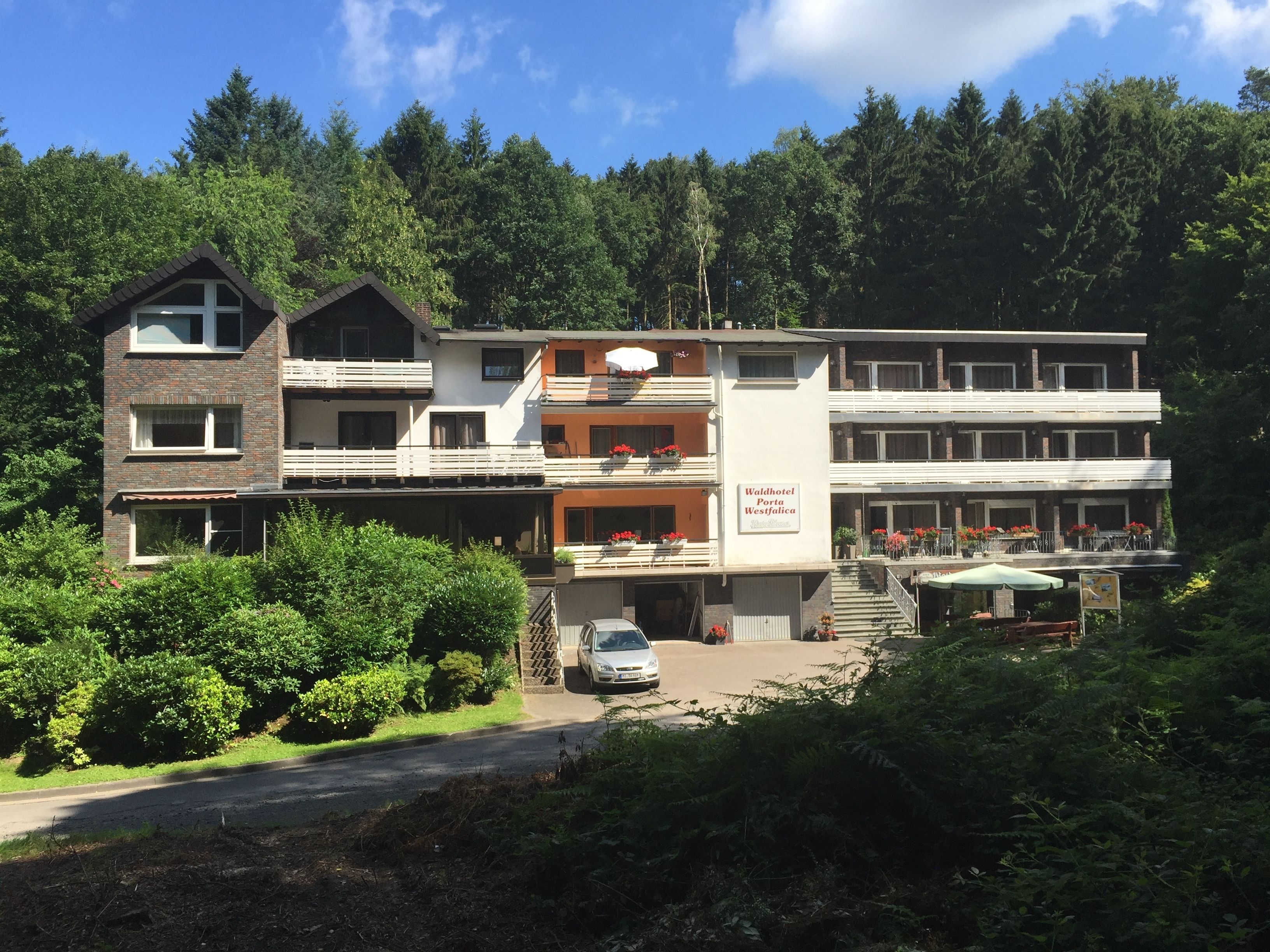 A hotel with multiple floors, outdoor seating, and a sign indicating it is a Waldhotel Porta Westfalica.