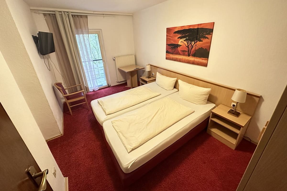 Une chambre d’hôtel avec un lit double, un bureau, une chaise, un téléviseur fixé au mur et un tableau représentant un arbre.