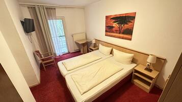 Una camera d'albergo con un letto matrimoniale, una scrivania, una sedia, una TV a muro e un quadro raffigurante un albero.
