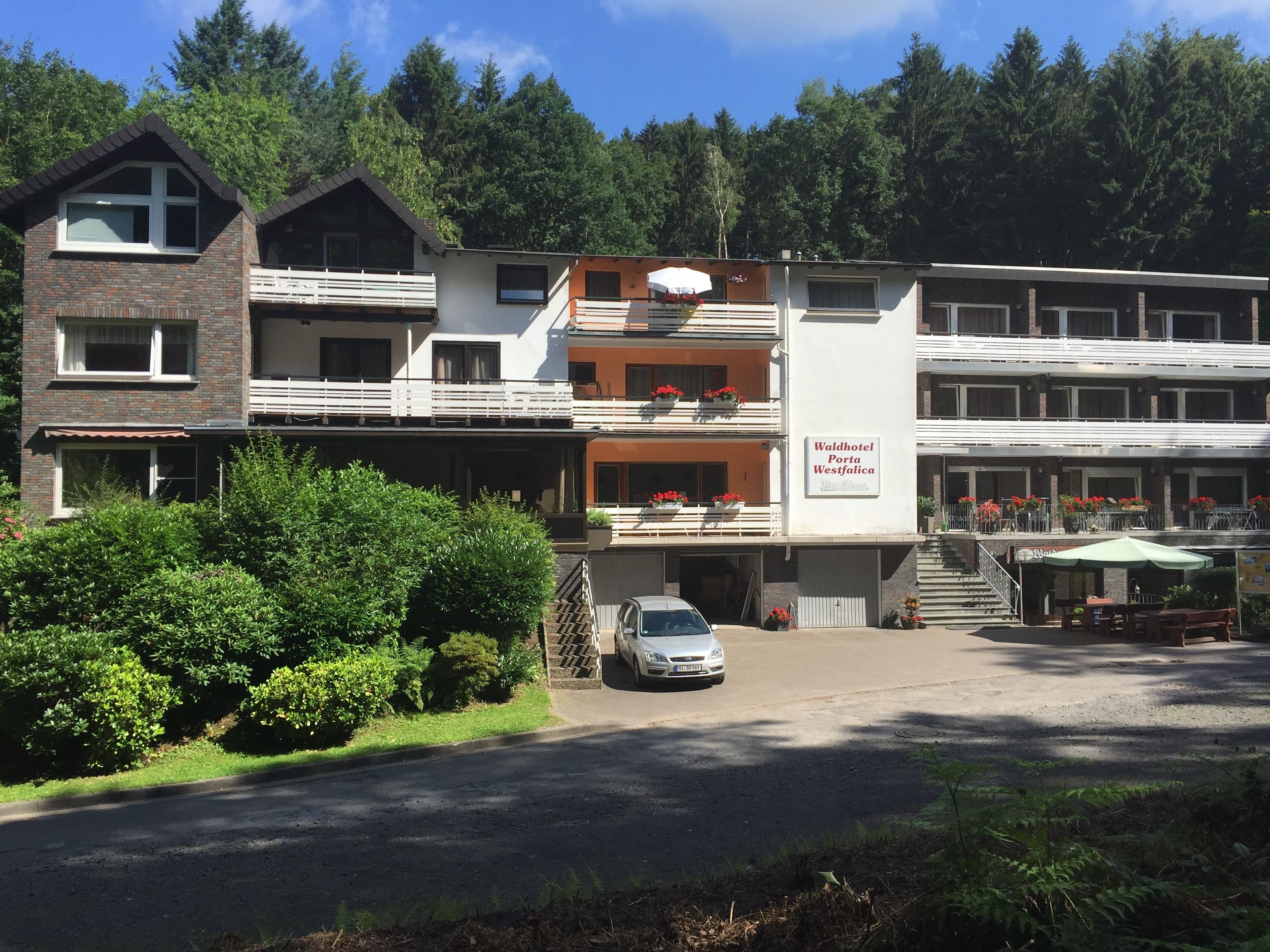 A multi-story hotel with balconies, a parking area, and a sign for 'Waldhotel Porta Westfalica'.