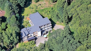 An aerial view of a multi-story building surrounded by dense forest. - Waldhotel Porta Westfalica garni (Porta Westfalica)