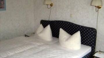 Una cama con edredón blanco y almohadas, cabecera oscura con estampado de lunares y dos lámparas fijadas a la pared.