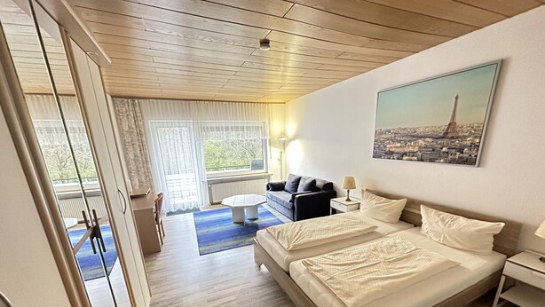 A hotel room with a bed, a sofa, a small table, and a painting of the Eiffel Tower. - Waldhotel Porta Westfalica garni (Porta Westfalica)