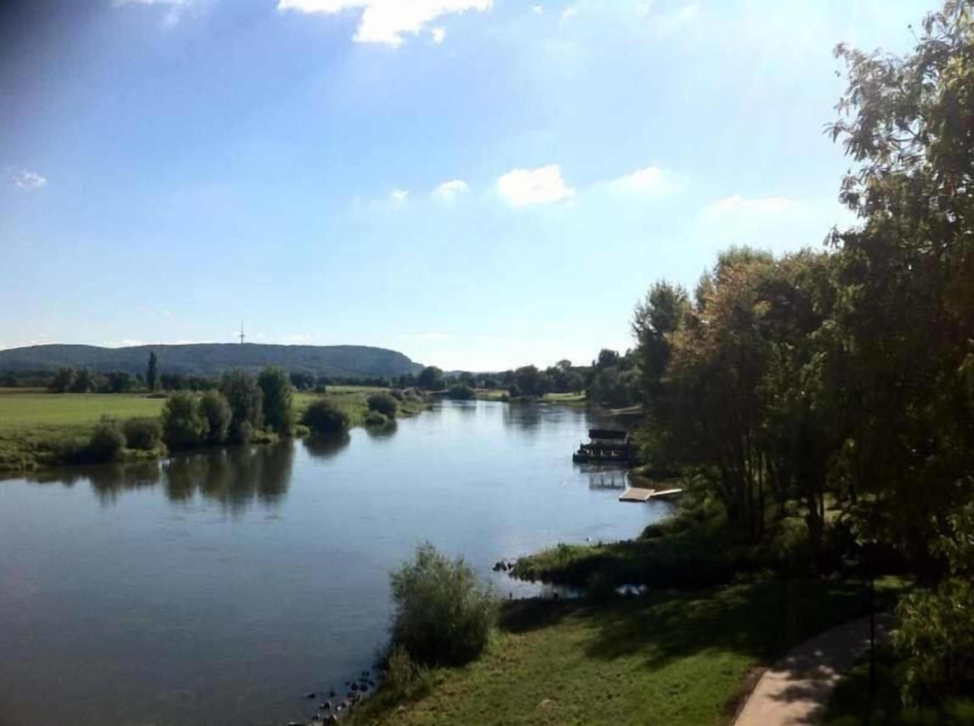 A river with a dock, surrounded by greenery and hills in the background.