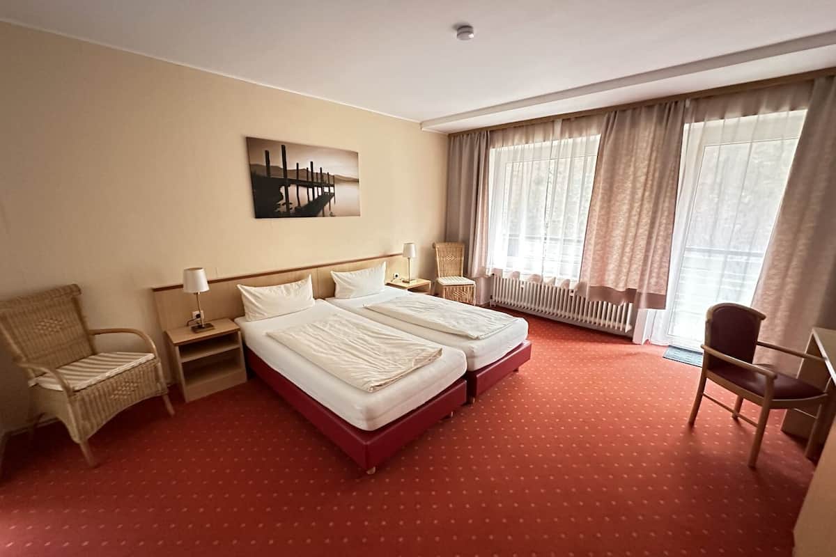 Une chambre d’hôtel avec deux lits, une chaise, un bureau, un radiateur et une fenêtre avec des rideaux.